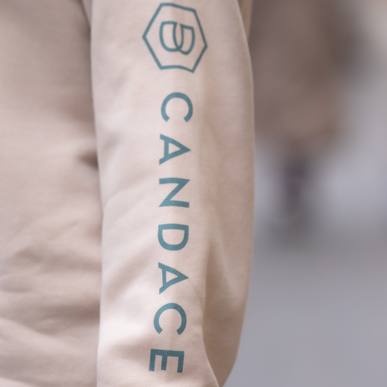 Beige SLEEVE with 'CANDACE' branding on a blurred background