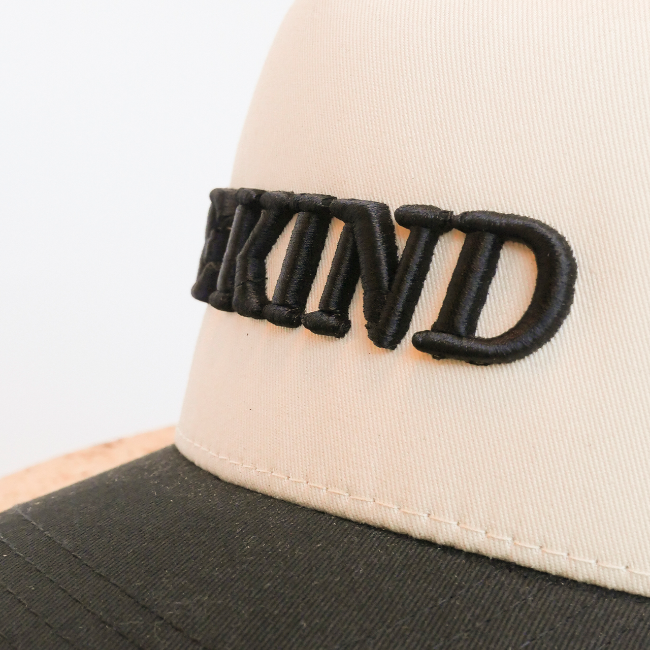 Close-up of a cap with 'BE KIND' embroidered on the visor against a white background