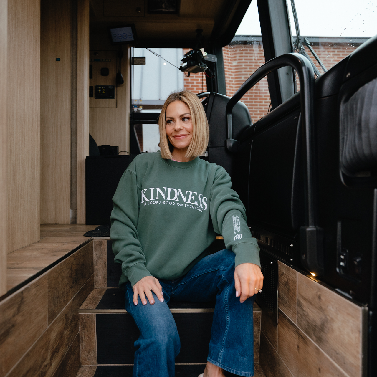 Woman wearing a green sweatshirt with 'KINDNESS' text inside a vehicle.