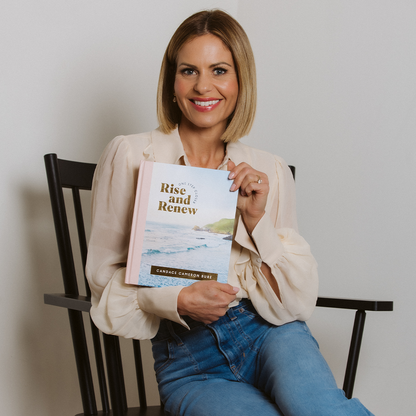 Woman holding a book titled 'Rise and Renew' while sitting on a chair.